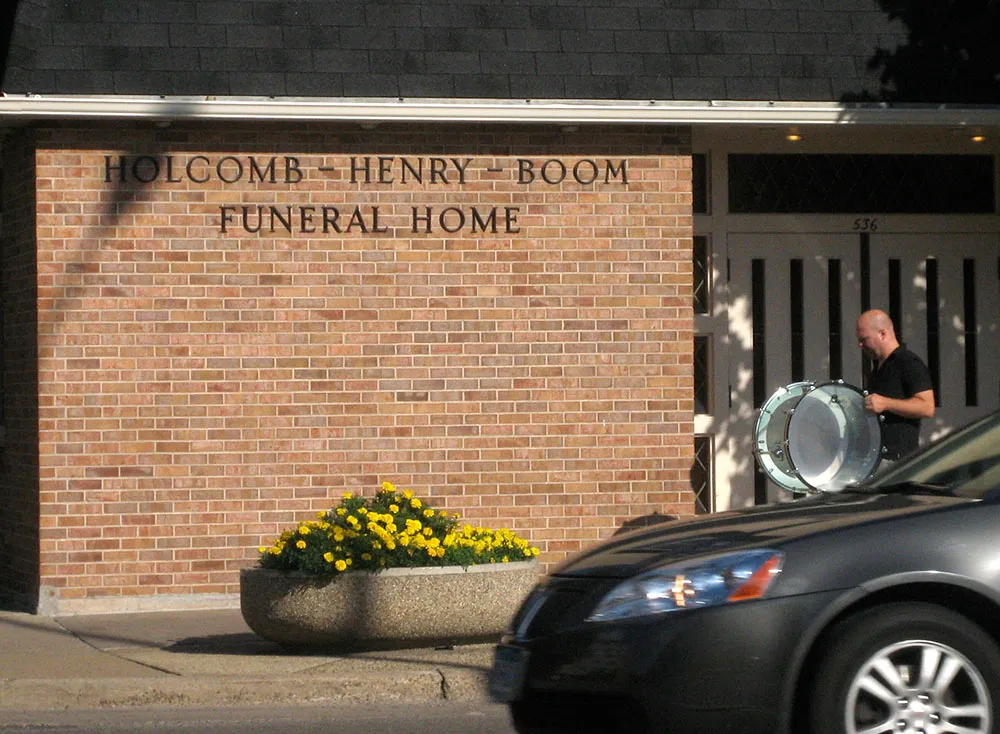 Bass drum player walks past the Holcomb-Henry-Boom Funeral Home.