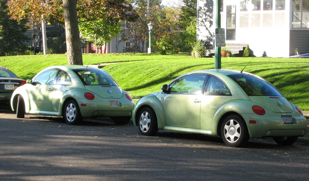 Blue, black and gray VW bugs in adjacent parking lot spaces.